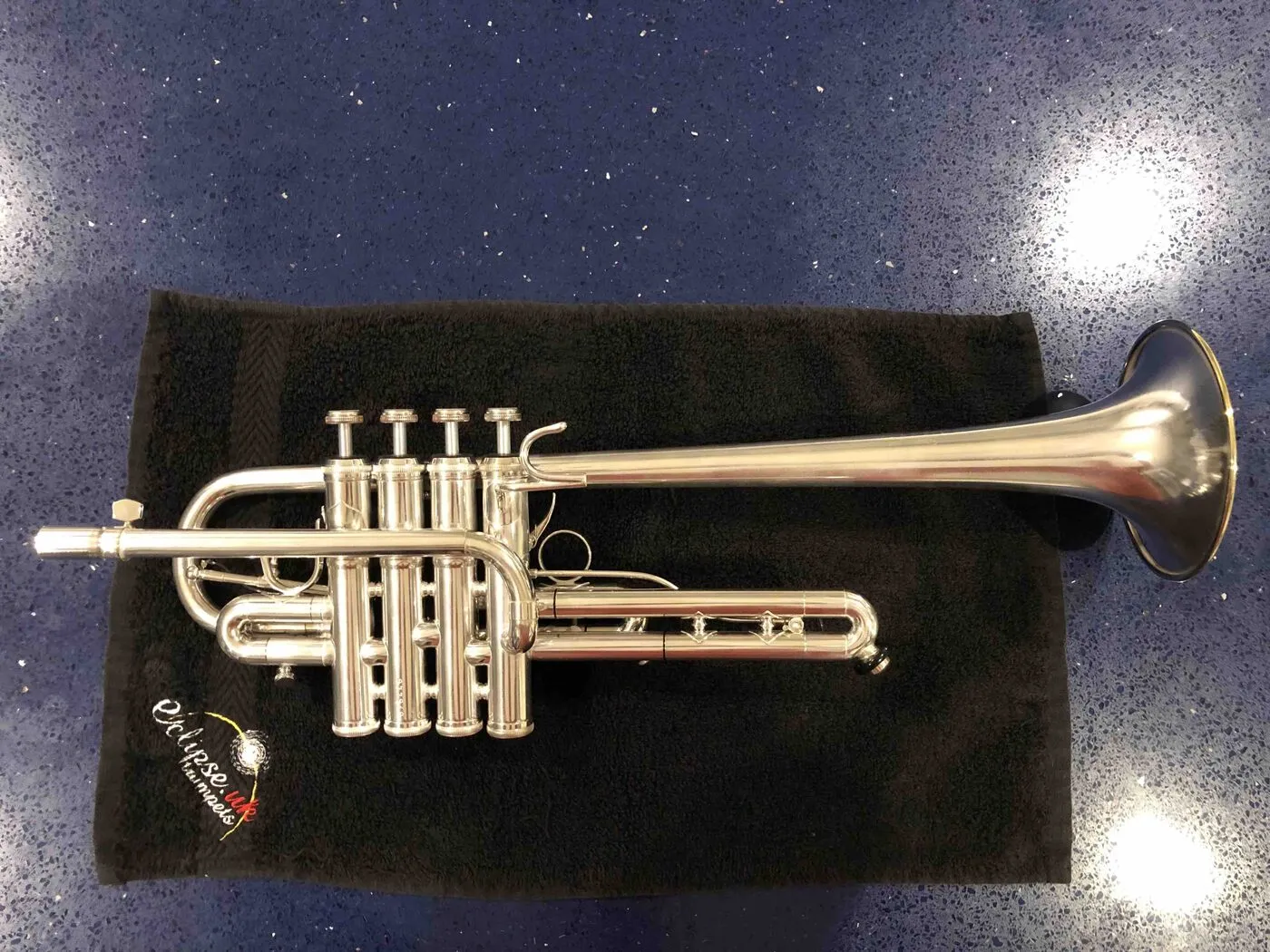 Silver E♭ trumpet with four piston valves resting on black cloth